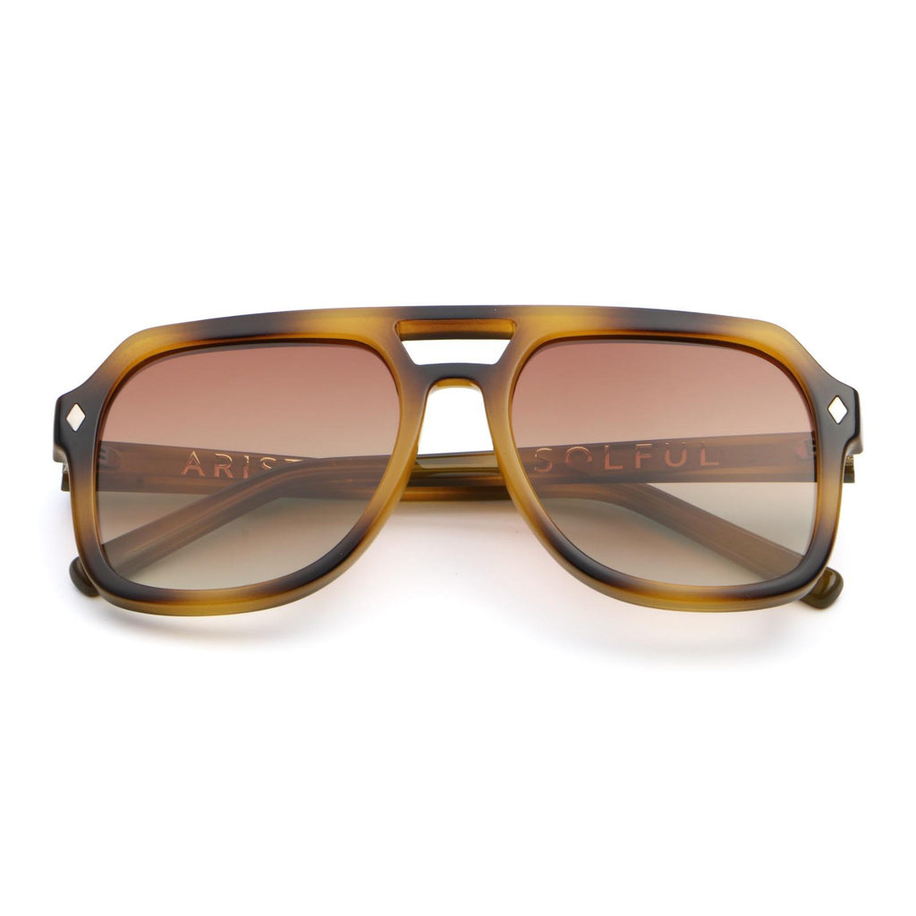 A pair of aviator-style sunglasses with a translucent tortoiseshell frame in brown and amber tones, featuring gradient brown lenses and the brand name 'SOLTUL' printed on the inner left temple arm.